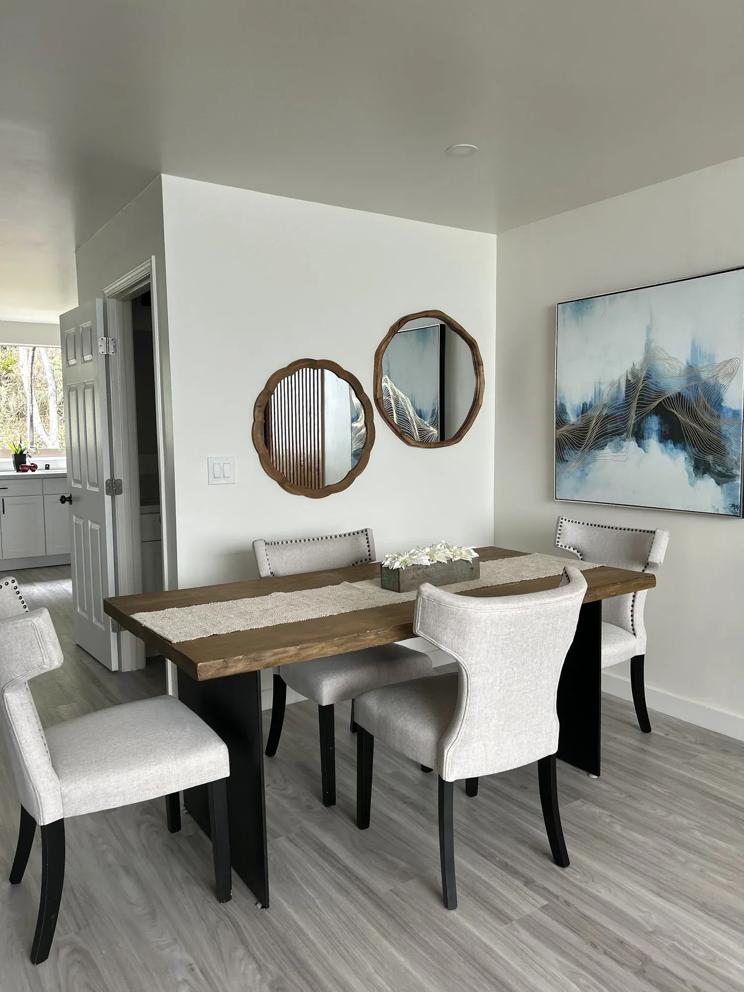 A dining room with a wooden table surrounded by six upholstered chairs with black legs, cozy modern dining table, and abstract artwork and mirrors on the wall.